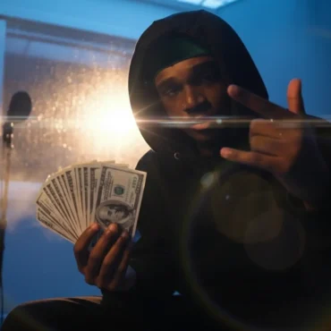 BLVD CO in studio hoodie, holding money stack, showing confidence.