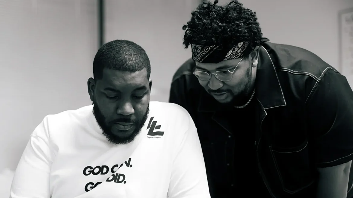 A black and white photo of two men, likely Oryan Latin and his brother JuiceDaCity, looking down at a smartphone together in a studio setting.