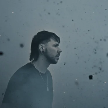 Seide stands in stormy chaos as debris floats around him, symbolizing struggle and strength.