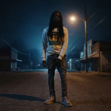 Foreign Izzy standing in a dark street at night under a street light.