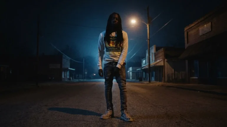 Foreign Izzy standing in a dark street at night under a street light.