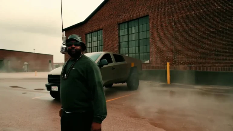 WizeTheChosen standing in front of a Cybertruck and a vintage microphone, wearing a bucket hat and sunglasses.