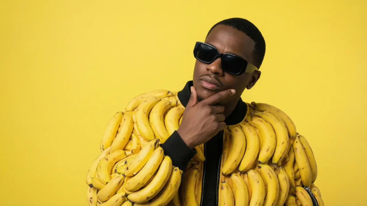 Black male hip hop artist wearing a bomber jacket made of yellow bananas thinking in front of a yellow background.