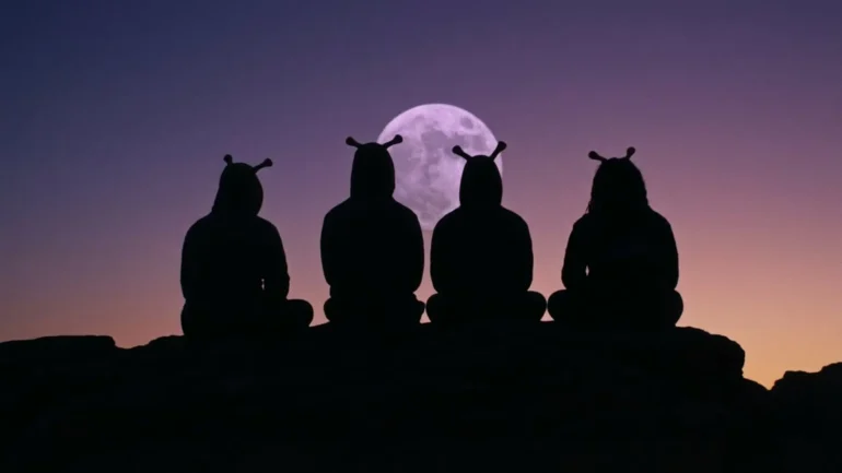 Four members of Space Cadets in alien costumes sitting on a rock silhouette against a purple moon and sunset.