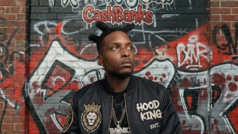 C.S.H. Banks wearing a black Hood King Ent bomber jacket against a graffiti wall.