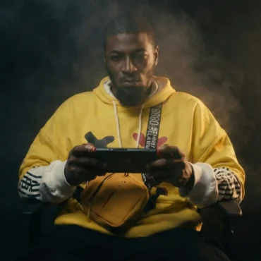 Musical artist Covay Fox wearing a yellow hoodie and holding a handheld gaming console.