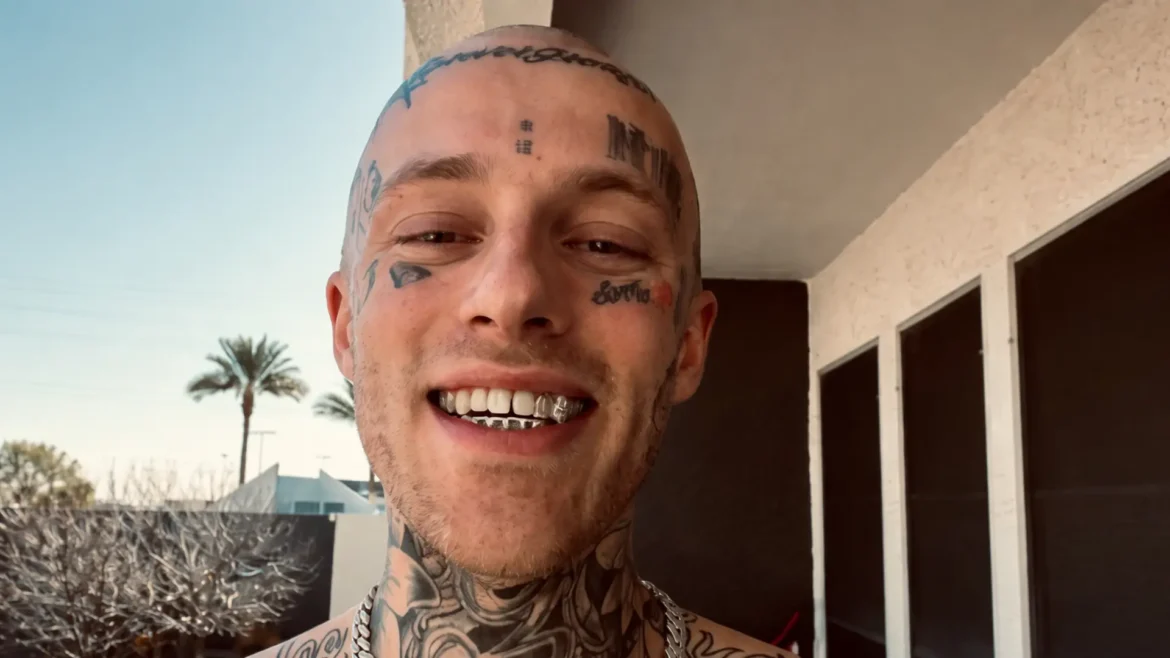 Rapper Free Zoey shirtless with face tattoos and silver grills smiling on a sunny balcony with palm trees in the background.