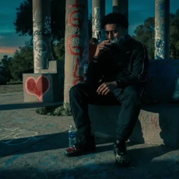 Lul Stackit sitting on a concrete bench with graffiti in Los Angeles at dusk.