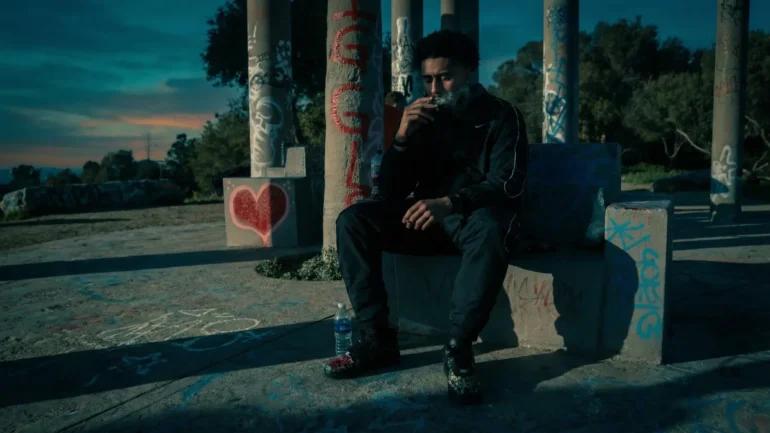 Lul Stackit sitting on a concrete bench with graffiti in Los Angeles at dusk.