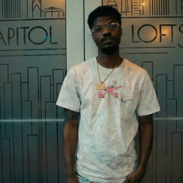 Richie Mike wearing a tie-dye shirt and glasses standing in front of Capitol Lofts glass doors.
