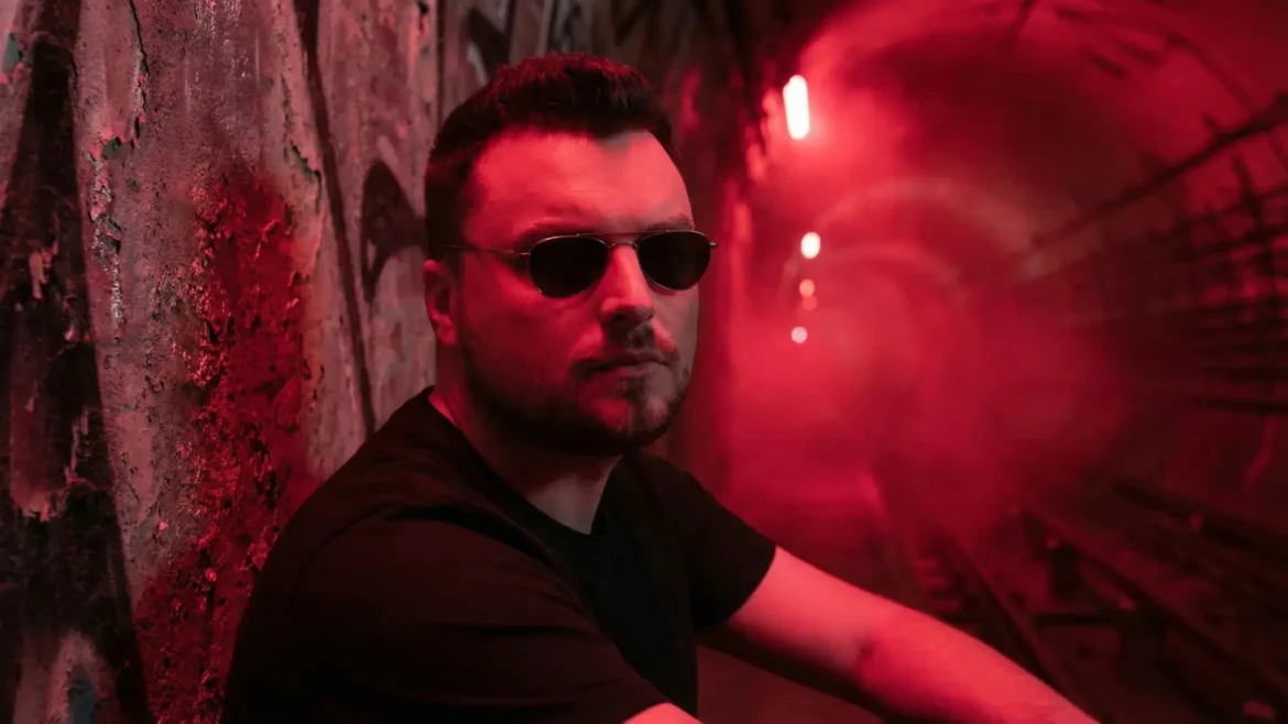 Ross Palmer wearing sunglasses in red neon lighting.