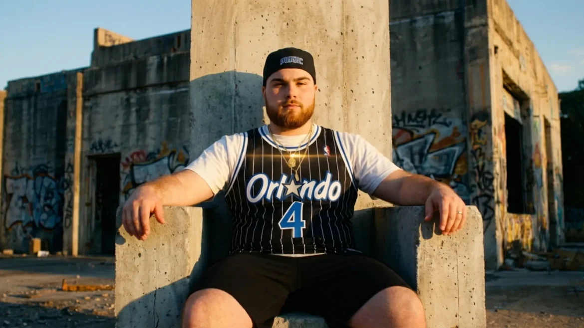 KJ Velo sitting on a concrete throne wearing an Orlando Magic jersey in an urban setting.