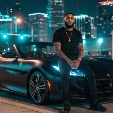 Nick Rob sitting on the hood of a matte black Ferrari at night with city skyline lights.