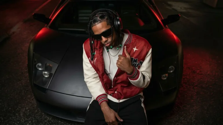 Artist Baby Draco leaning on a matte black Lamborghini Murciélago.