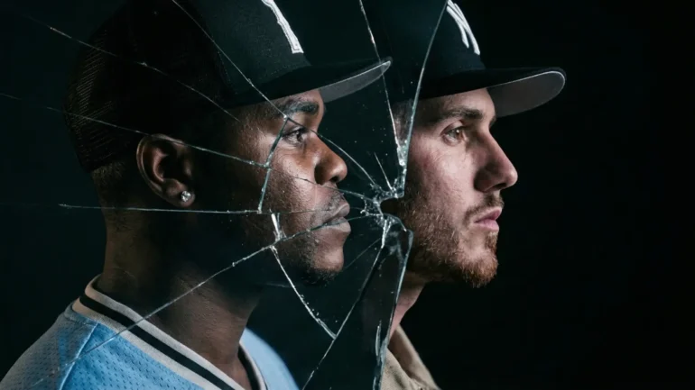 Two men in baseball caps viewed through cracked glass.