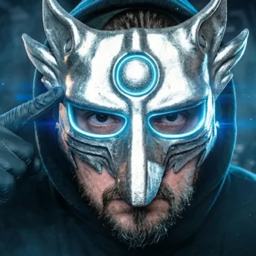 A man in a black hoodie wearing a detailed silver metal wolf mask with glowing blue eyes, pointing to his head.