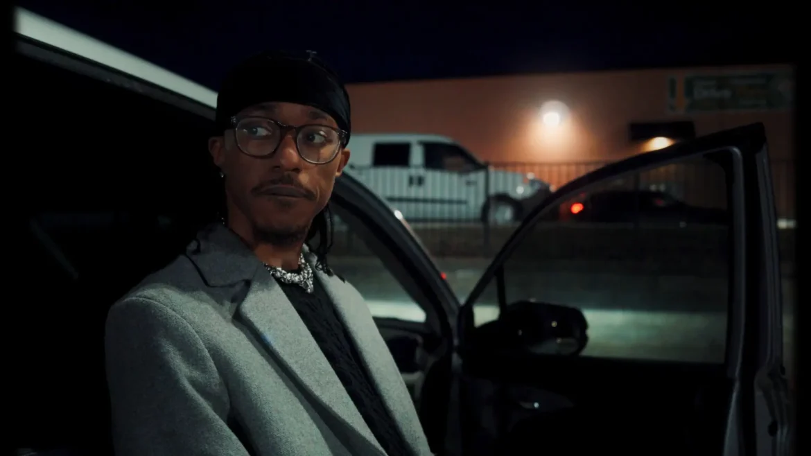 Artist JHN JSPH in a gray coat and glasses standing by a car at night.
