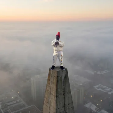 Musical artist Laf822 standing on a high concrete pillar overlooking a foggy city skyline.
