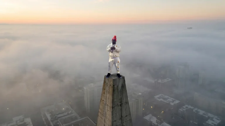 Musical artist Laf822 standing on a high concrete pillar overlooking a foggy city skyline.