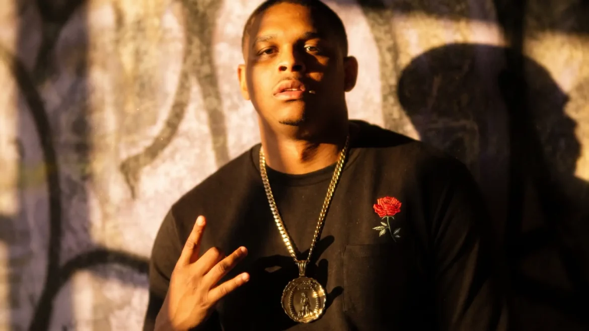 agboy Blu in a warm-lit close-up, throwing a hand sign near his chest, direct gaze into the camera, promoting "Same 24"