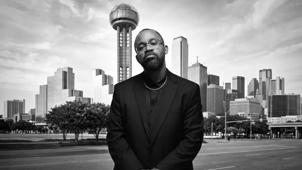 Jay Hallic in a black suit and open dress shirt, glasses, thin chain necklace, standing arms clasped, direct gaze at camera, black-and-white, downtown Dallas skyline and Reunion Tower behind him