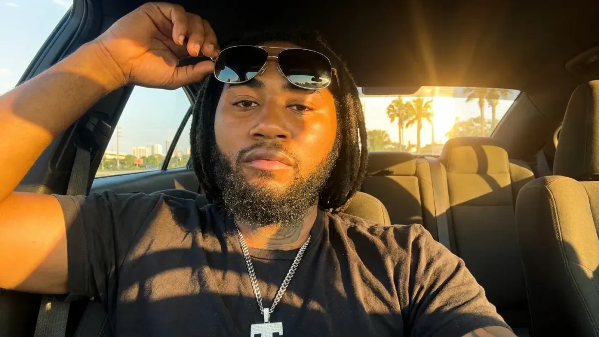TsuMan sitting in a car at sunset, one hand pushing sunglasses up, wearing a black tee and silver chain necklace, promoting his track "Getting"