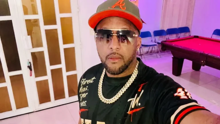 Kaaine in a cap with a red A logo, tinted gold-frame sunglasses and a gold Cuban link chain, taking a selfie in a room with a red pool table, for the track I'M HIM (Remix)